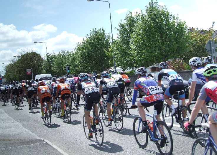 Peloton of cyclists in colorful jerseys riding on a road during a race. View from the back.